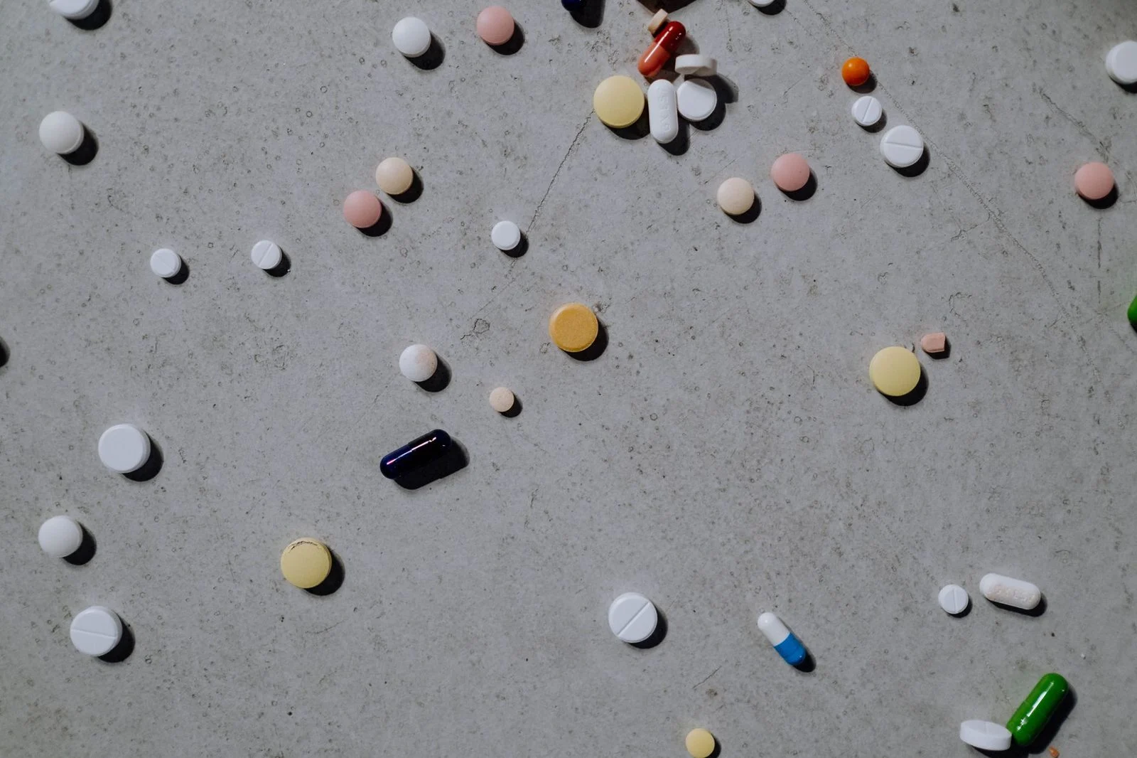Colorful prescription pills and tablets scattered on a grey surface.