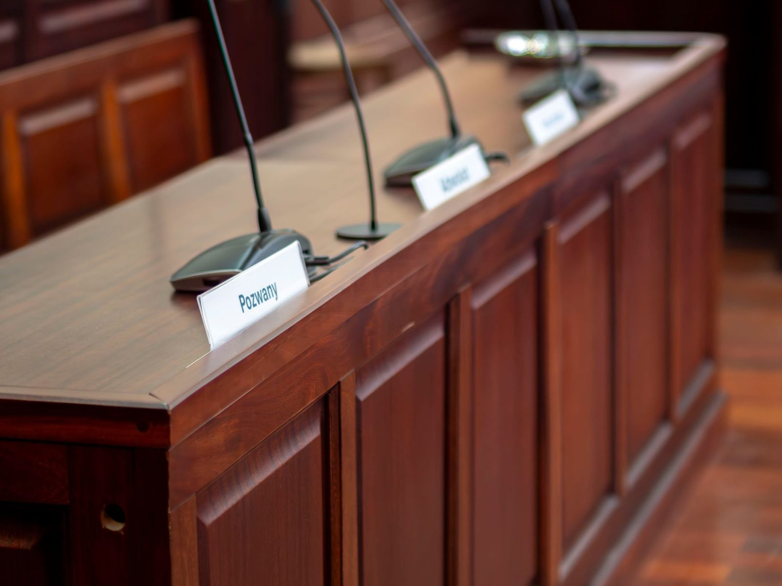 Escritorio vacío de sala de audiencias con micrófono y placas de identificación en tribunal.