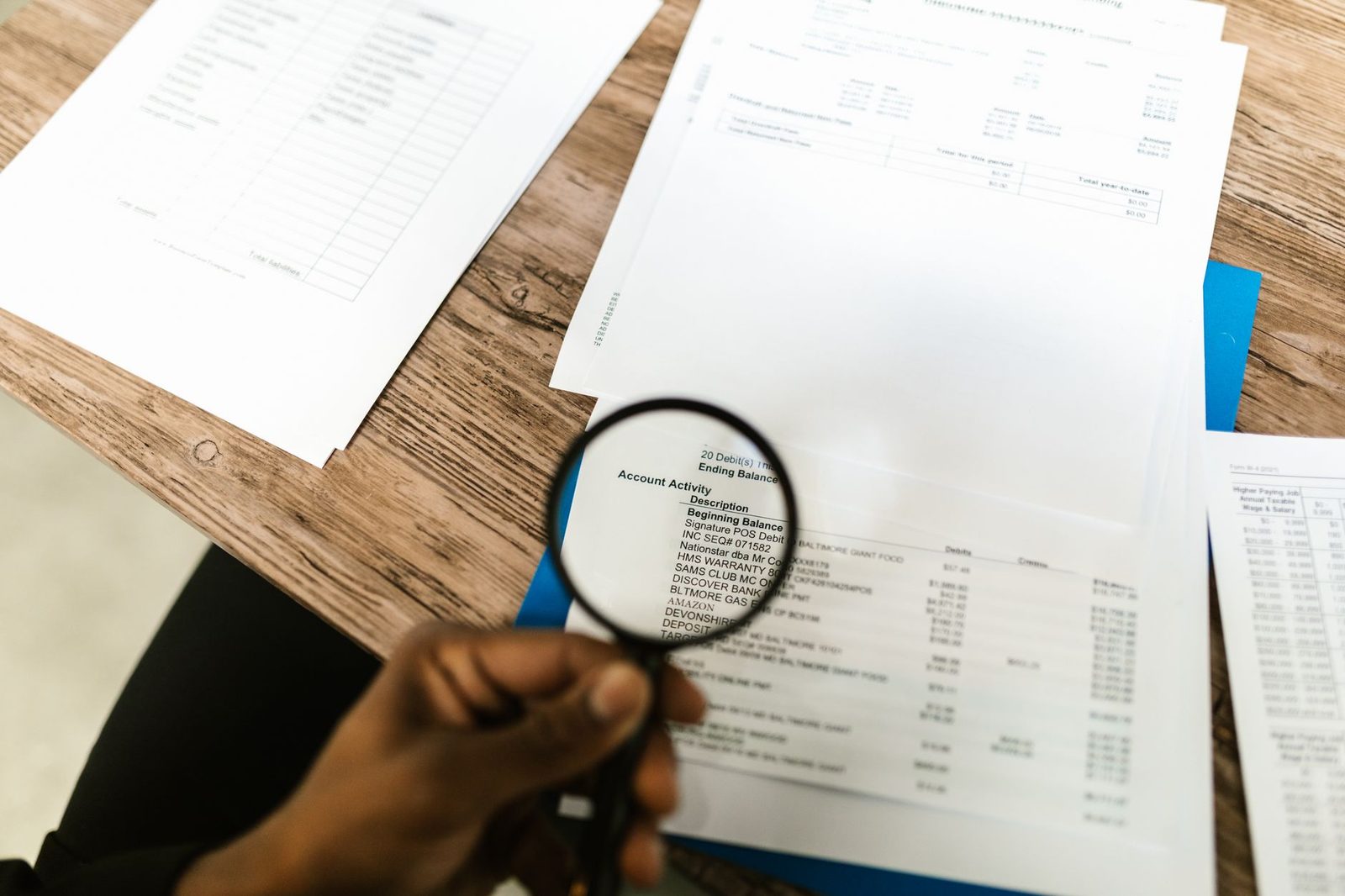 Hand with magnifying glass examining financial documents and records.