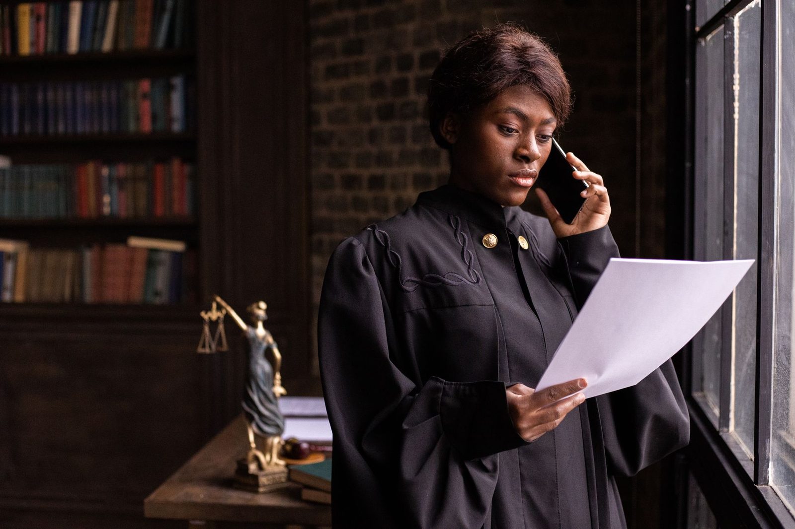 Judge in robe reviewing documents while on phone in office.