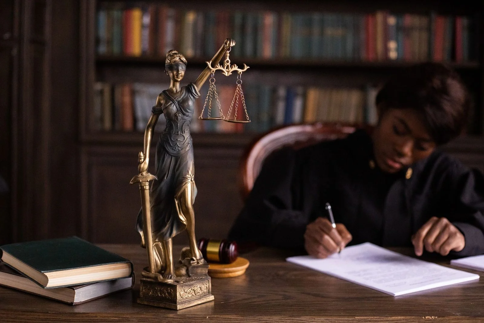 Judge writing legal documents at desk with Lady Justice statue.