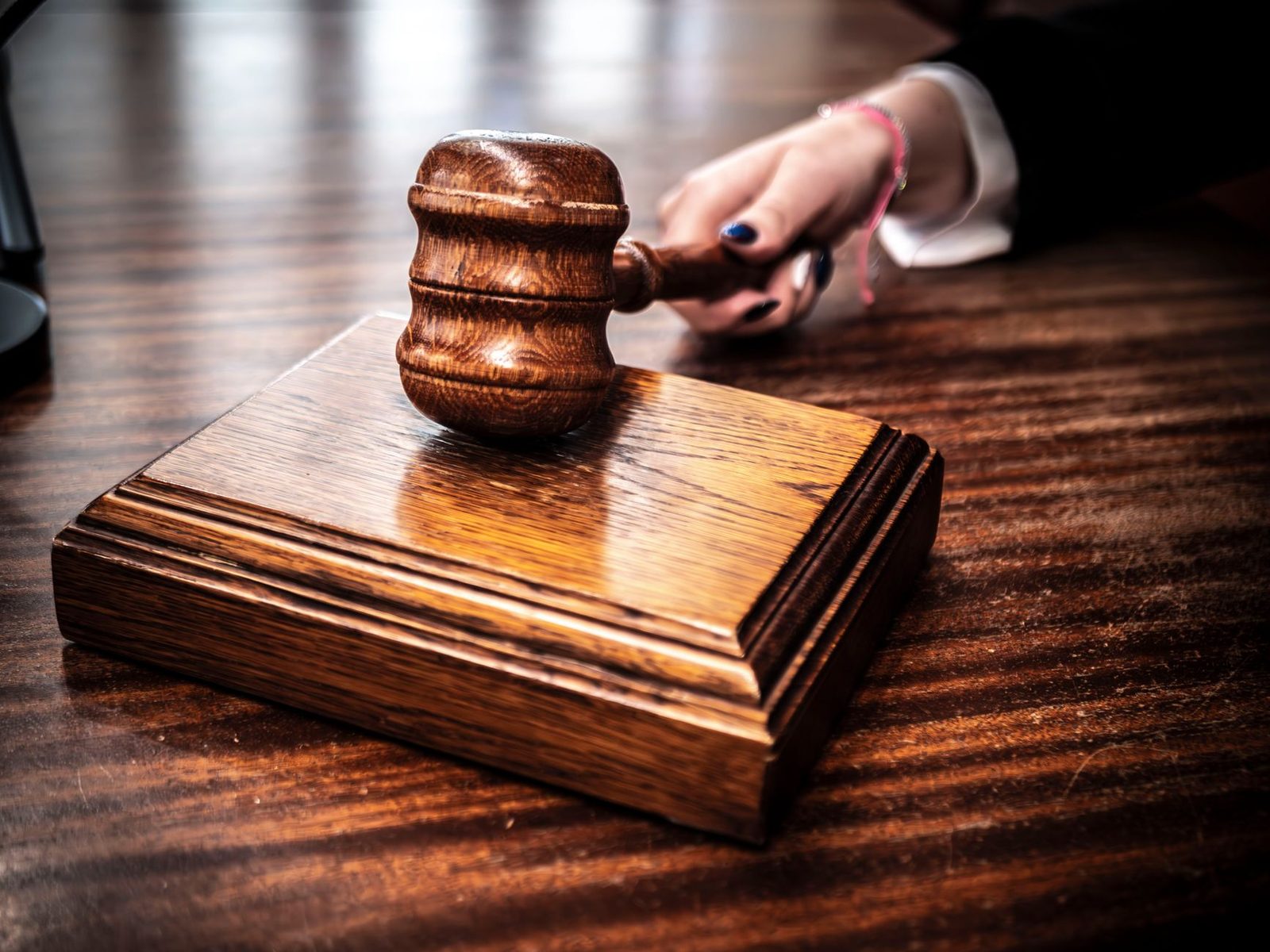 Wooden gavel in judge's hand at courtroom desk.