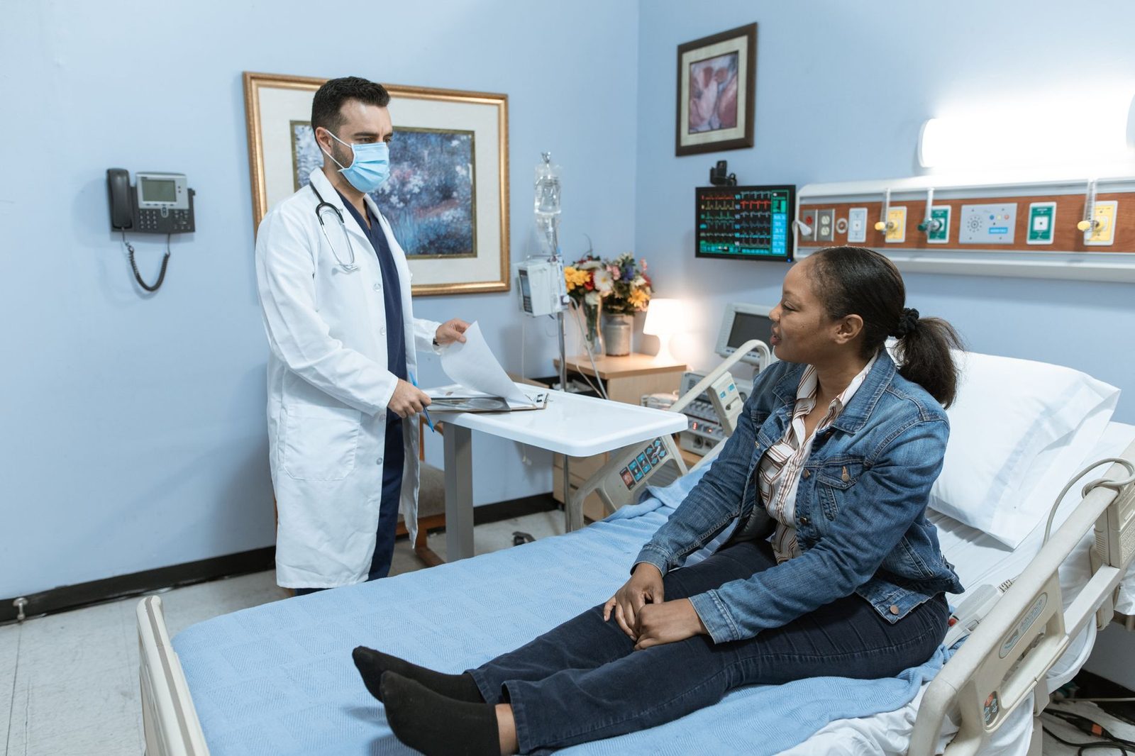 A doctor in scrubs examines a patient during a check-up in a hospital room.