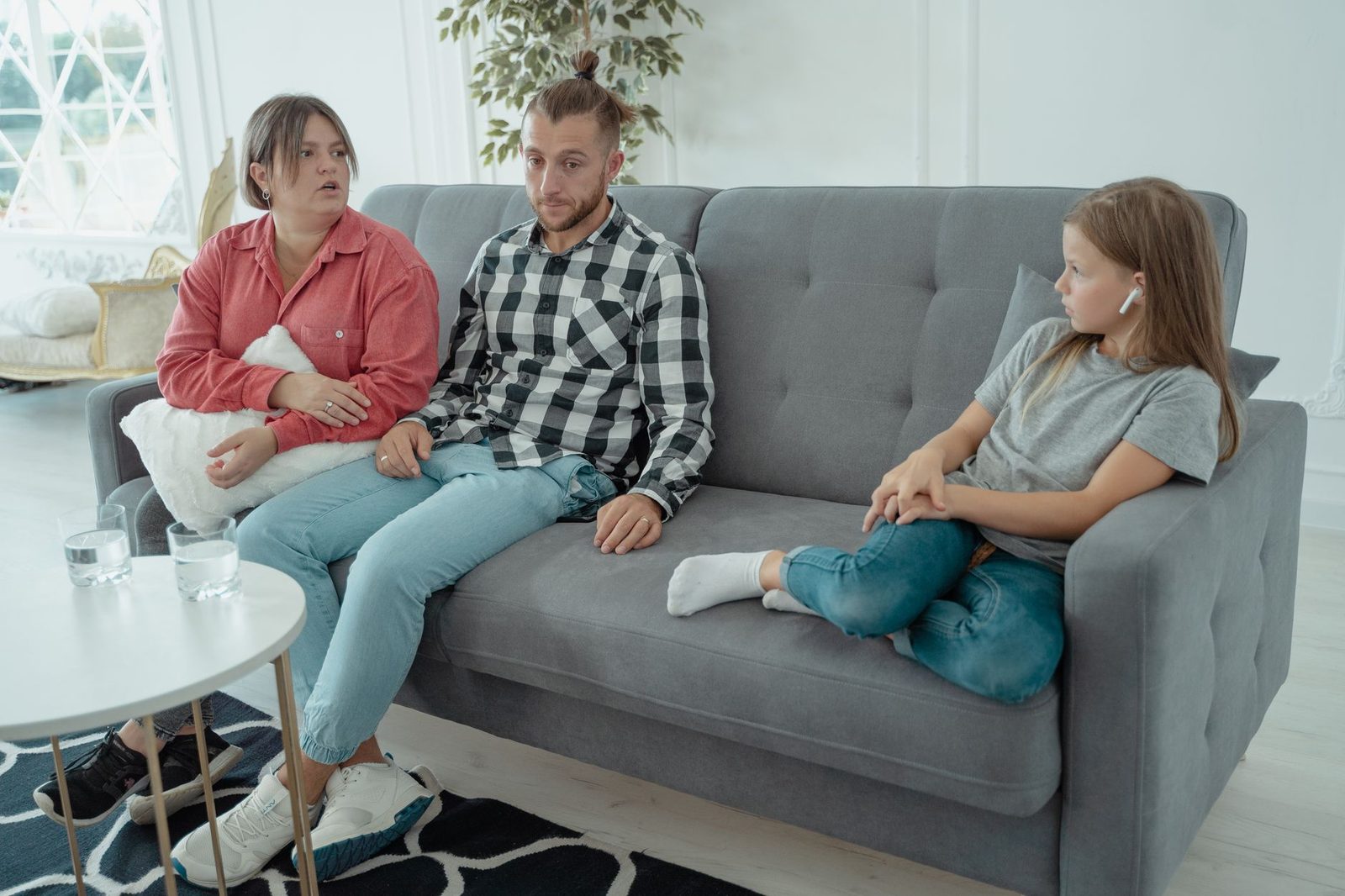 A family sits together on a sofa in a comfortable living room, appearing to talk through a difficult conversation.
