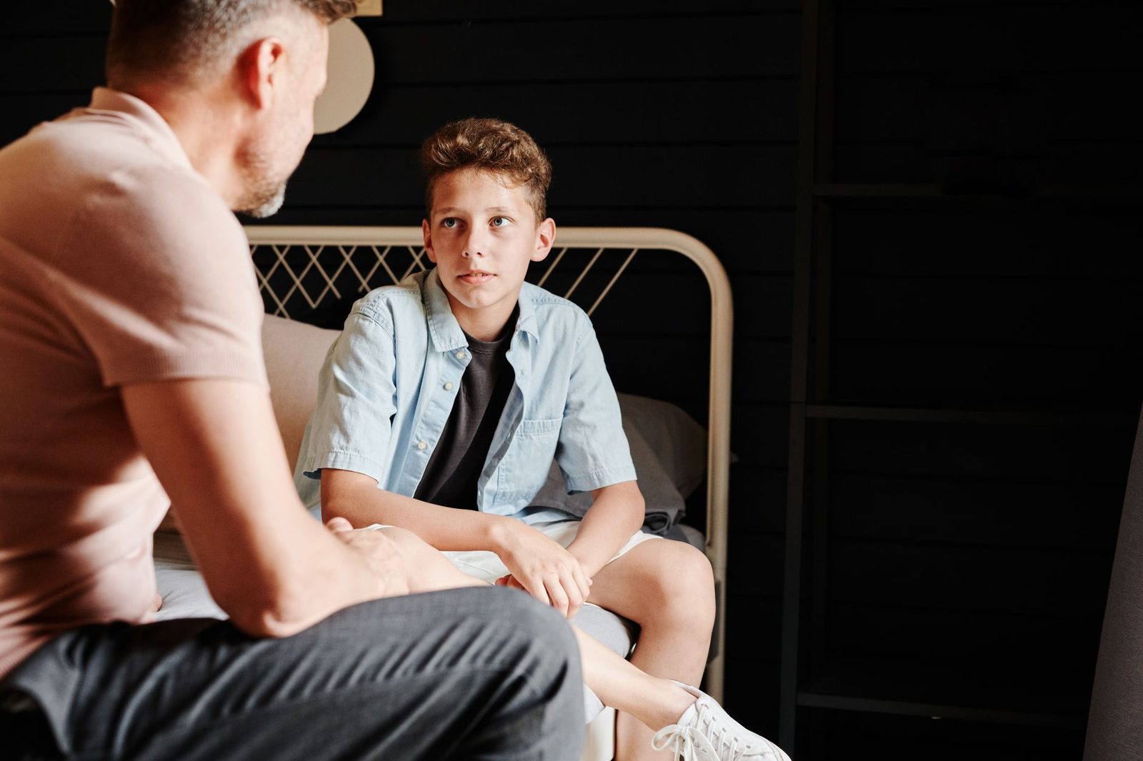 A father and adult son sit together indoors, engaged in a serious, heartfelt conversation.