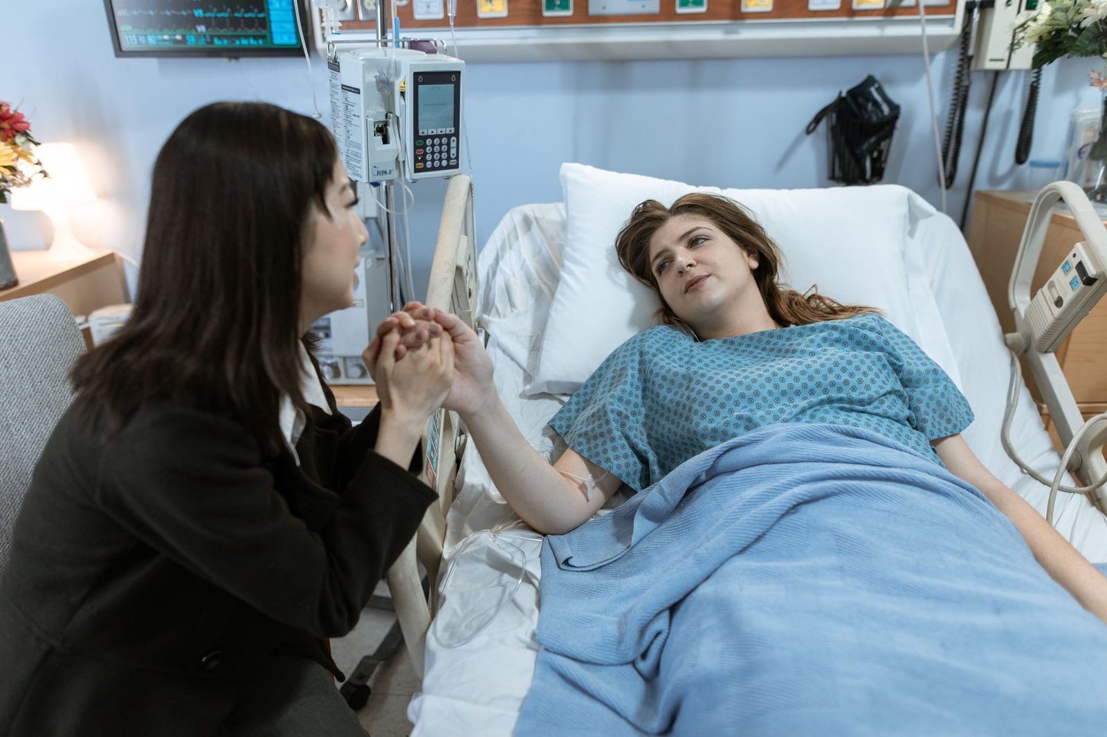 A friend sits beside a patient in a hospital bed, offering comfort and support.