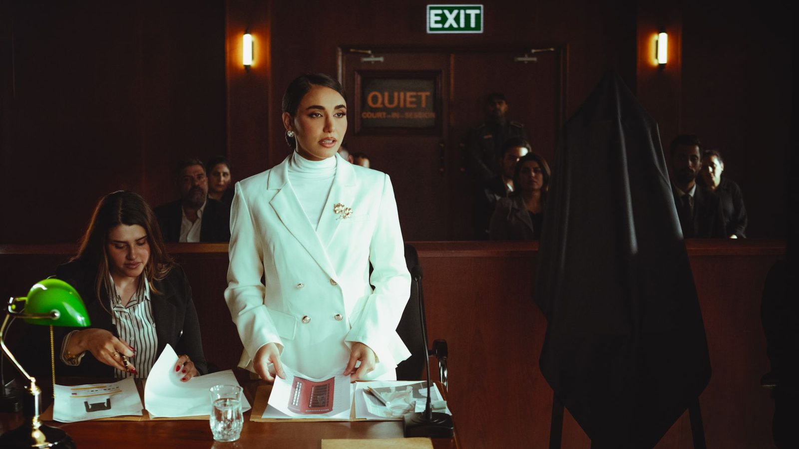 A lawyer in a white suit presents a case to colleagues in a courtroom.