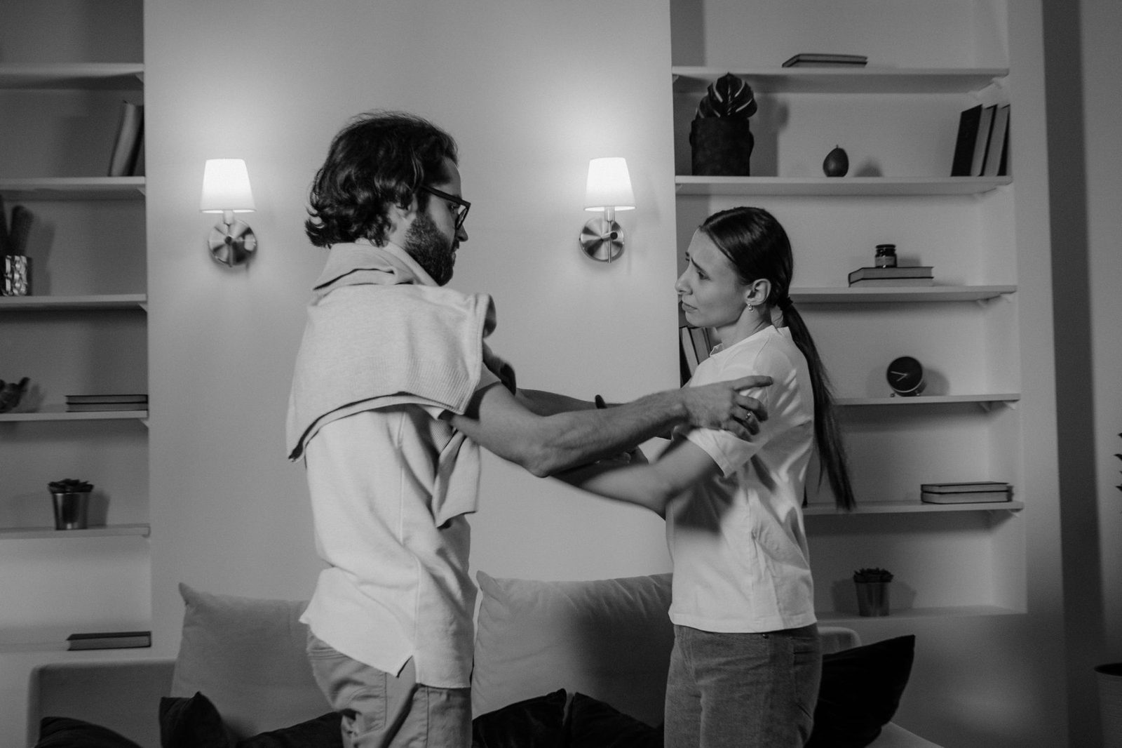 Un hombre y una mujer conversan seriamente, sentados frente a frente en un interior, en blanco y negro.