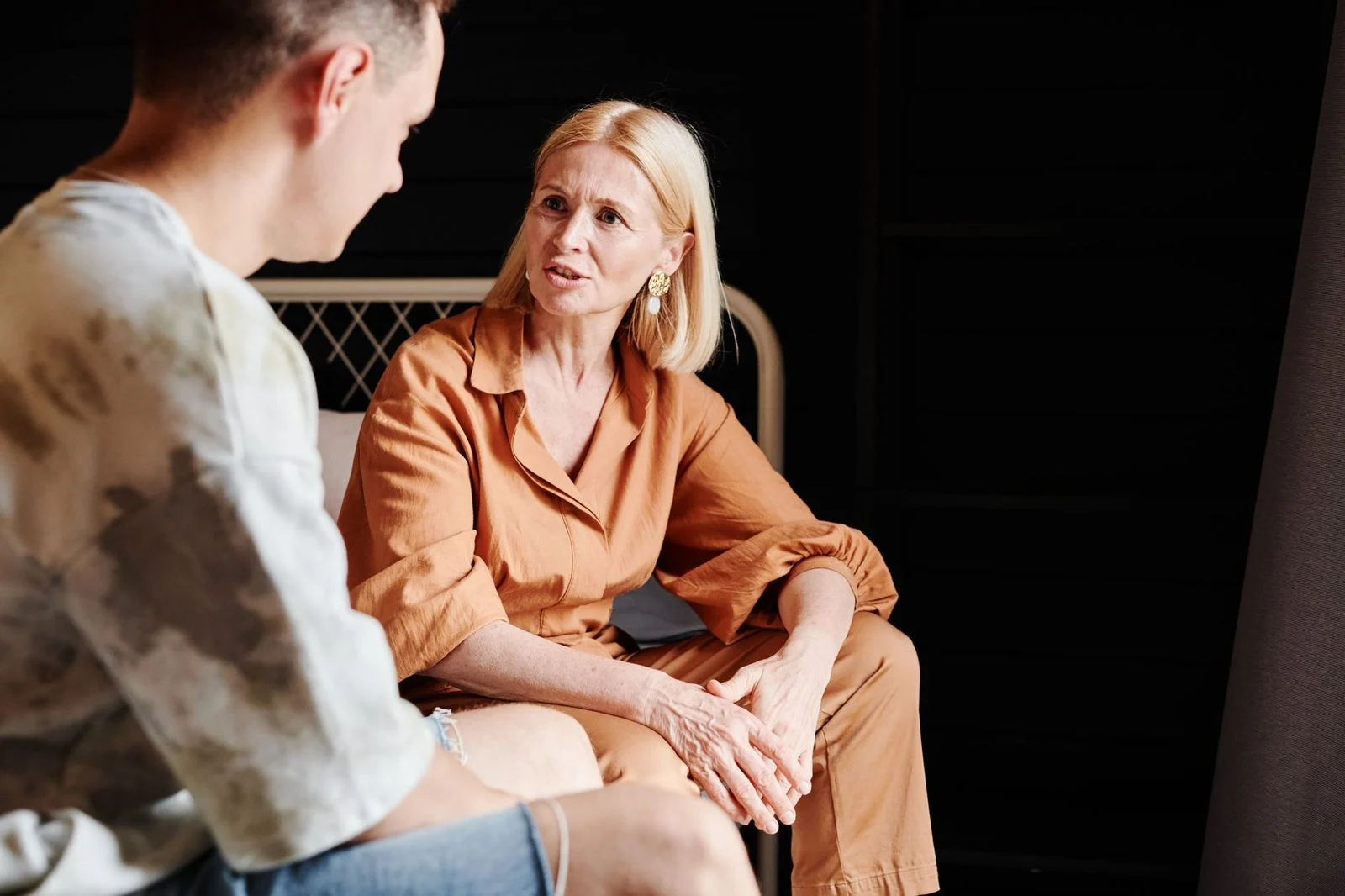 A mother and adult son sit close together in a living room, talking earnestly.