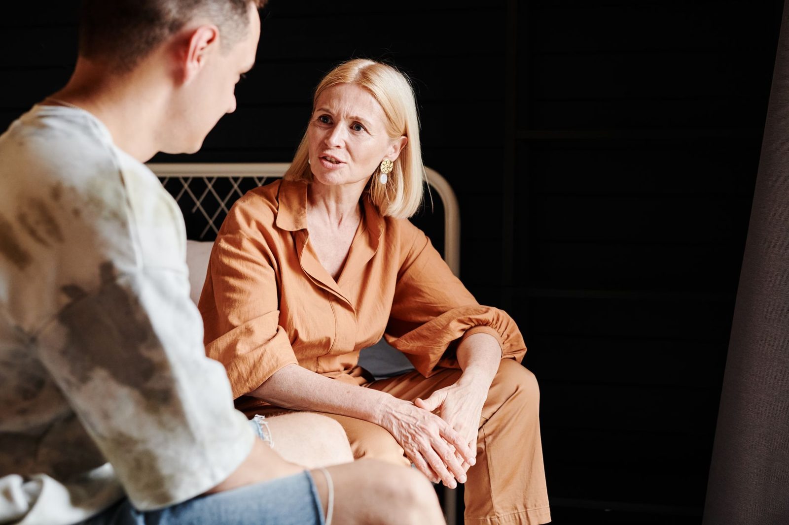 A mother and adult son sitting indoors, talking closely in a heartfelt conversation.