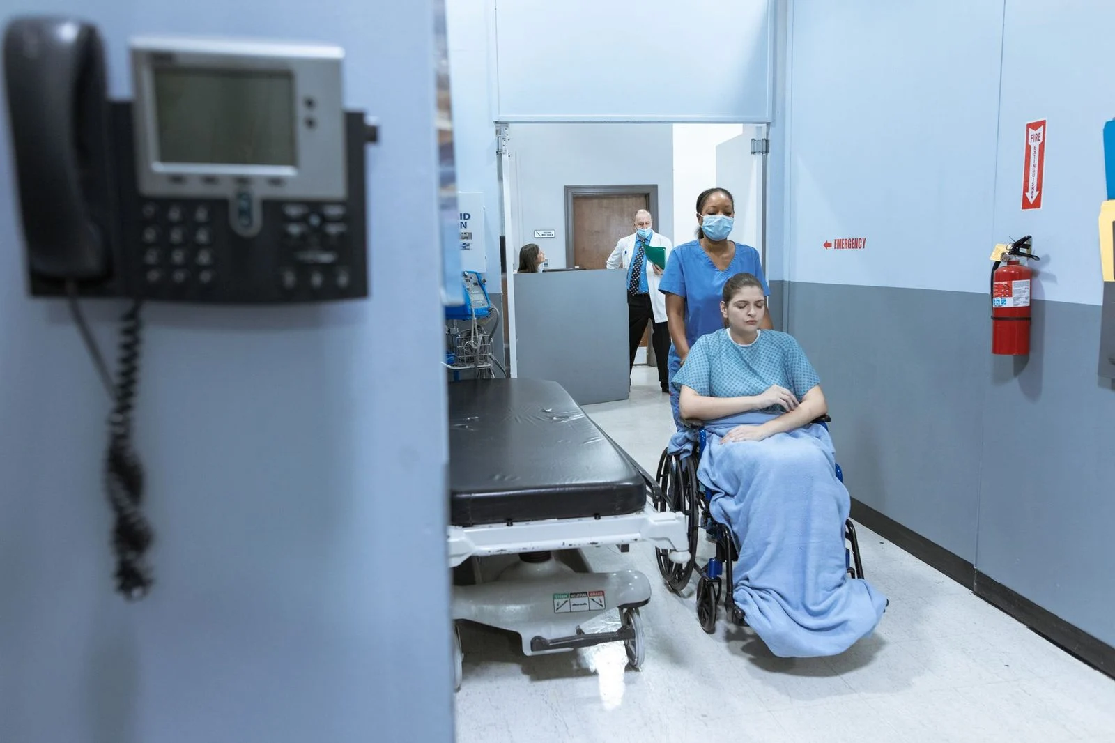 Una enfermera empuja a un paciente en silla de ruedas por un pasillo de hospital.