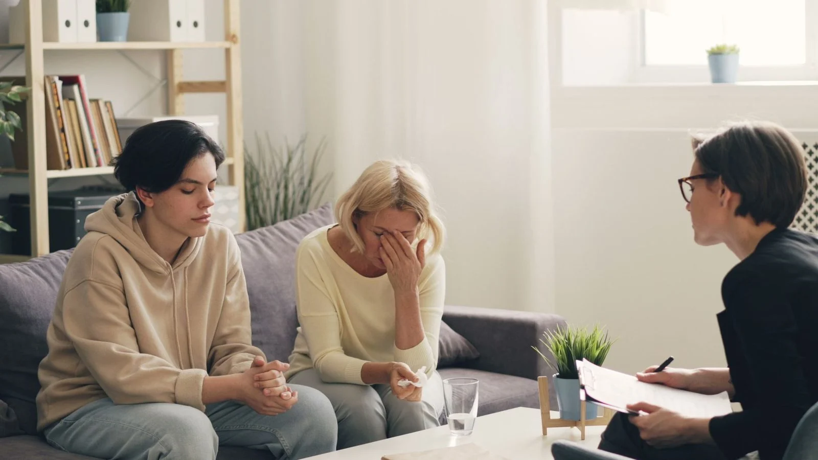 A therapist sits with a mother and adult son in a bright office, sharing a supportive conversation.