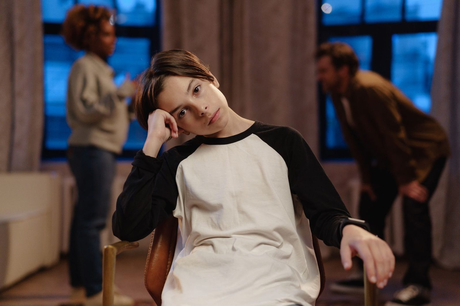 A young boy in a black and white shirt looks sad while his parents argue behind him.