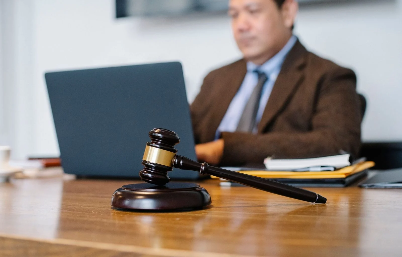 Asian man in formal attire seated at a desk in a law office, working on a netbook.