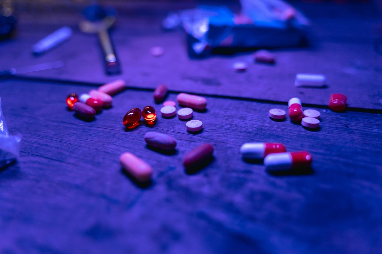 Assorted capsules and pills scattered on a wooden surface under blue lighting.
