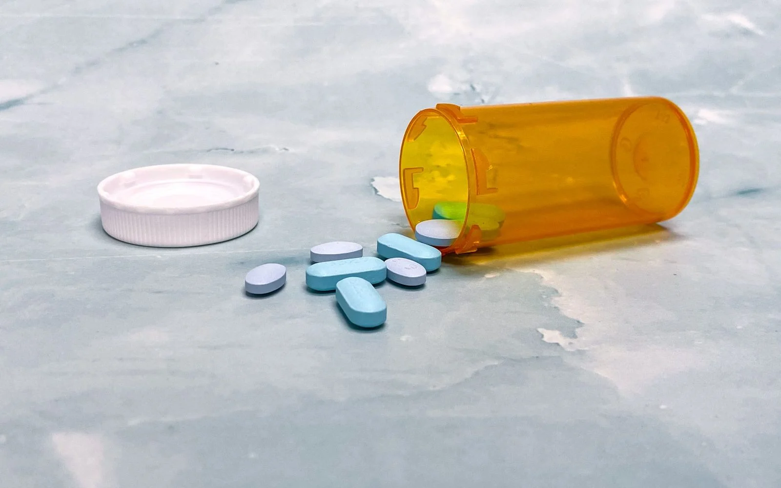 Blue pills spill from an orange prescription bottle onto a light surface.