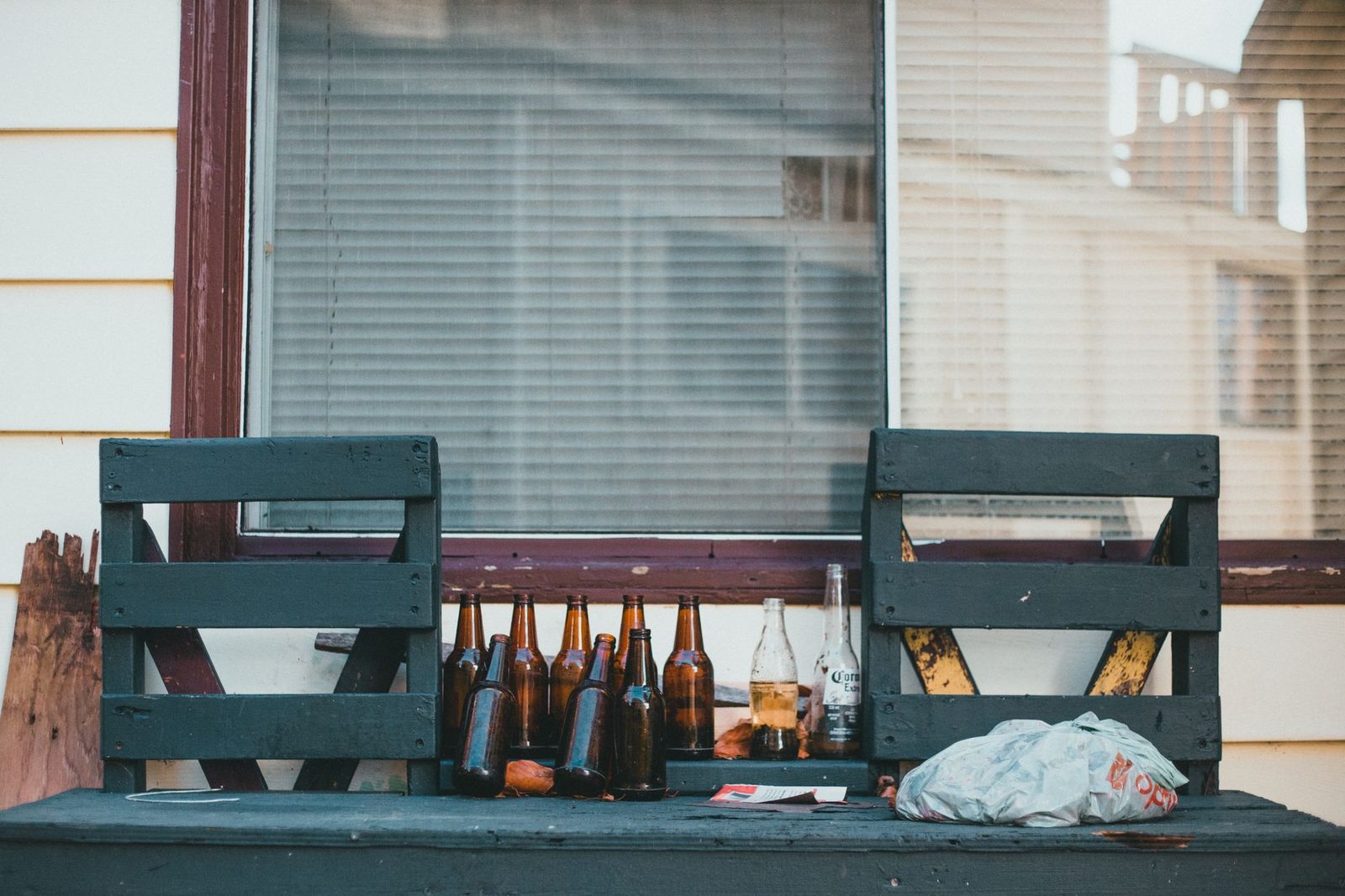 Botellas de cerveza vacías sobre banco rústico al aire libre.