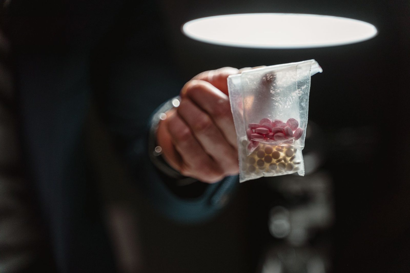Close-up of a hand holding a bag of assorted pills under harsh lighting.