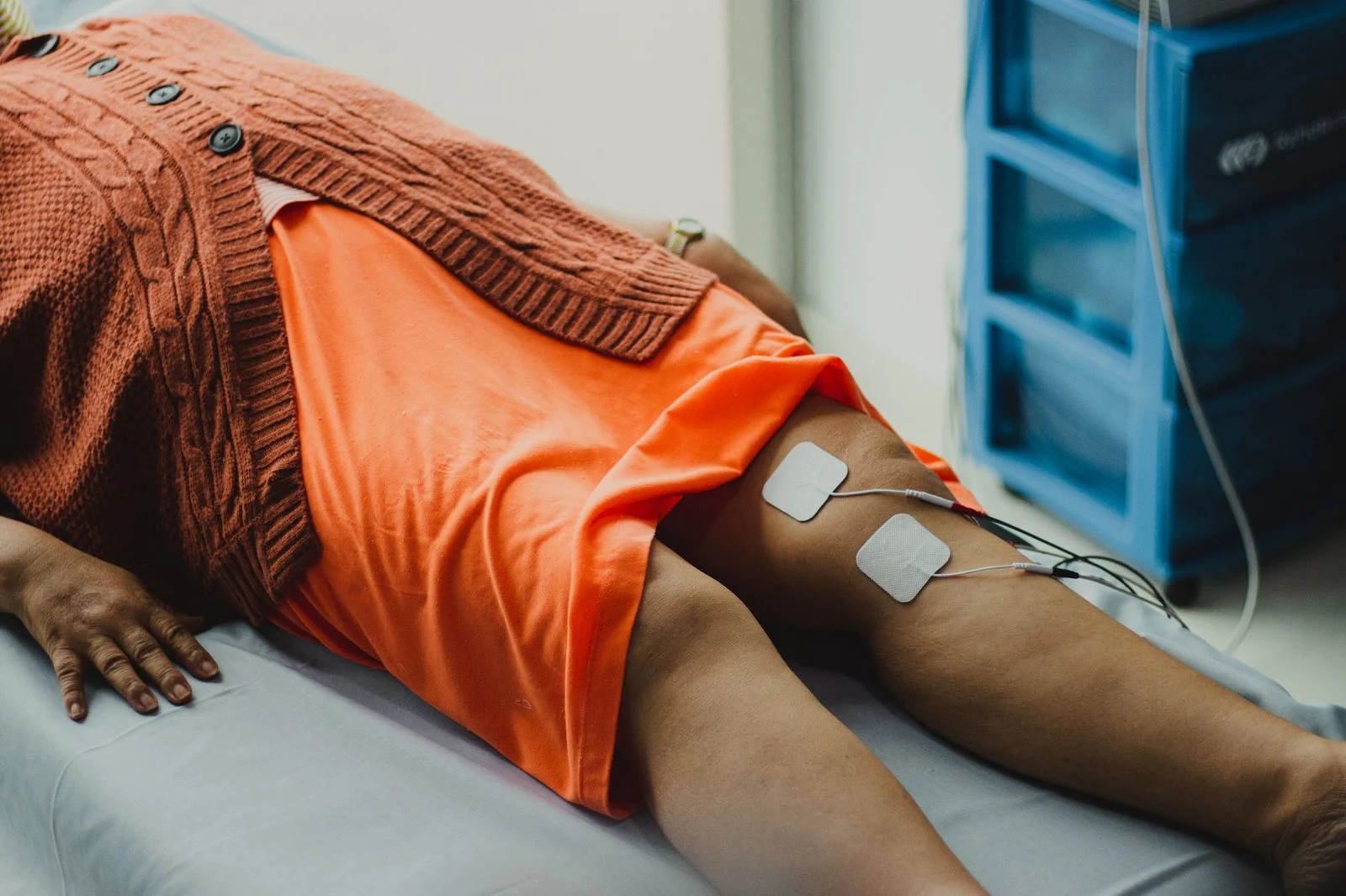 Close-up of a woman's legs receiving electrical therapy treatment in a hospital room.