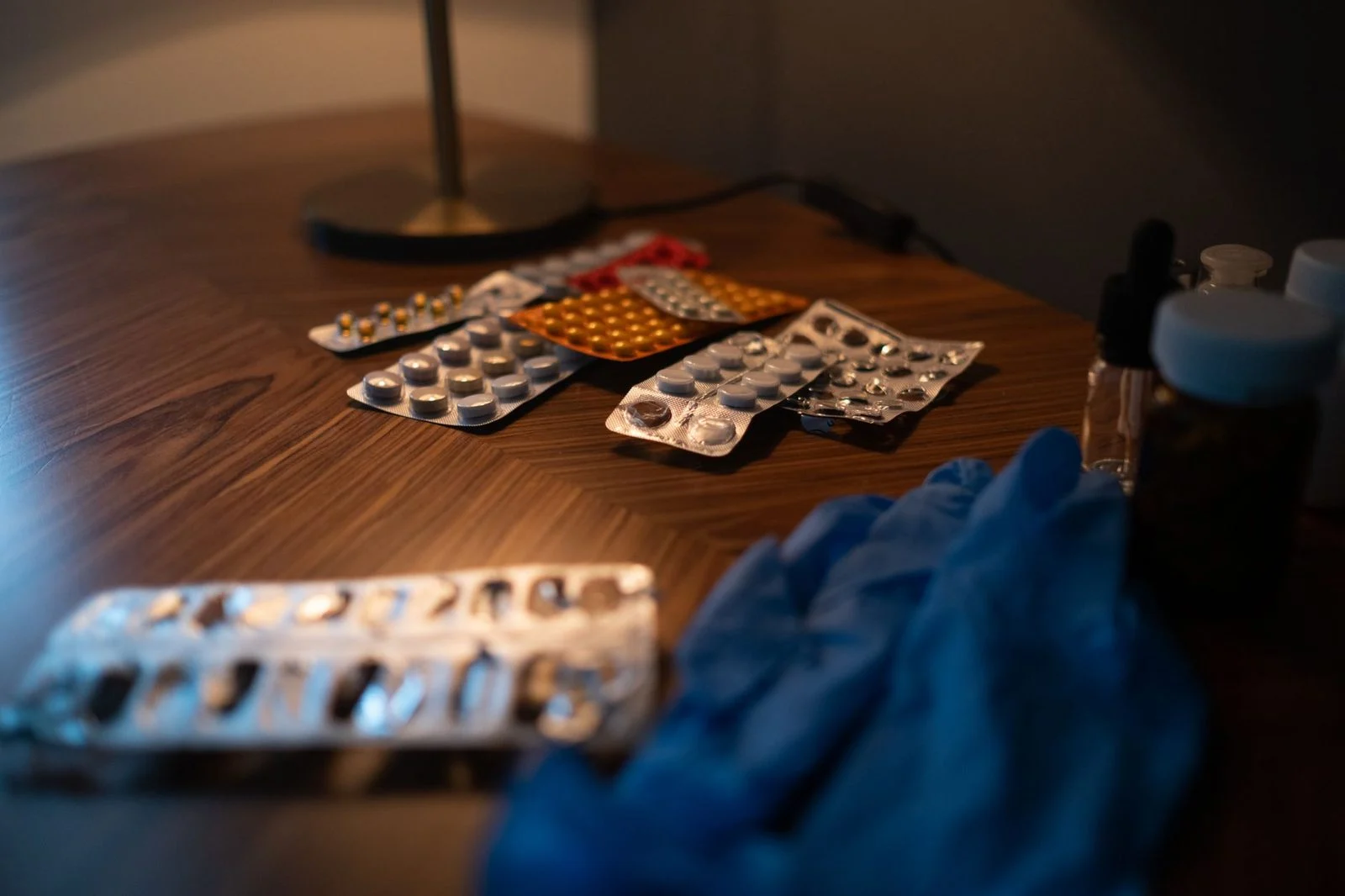 Close-up of medication blister packs and gloves resting on a wooden table.
