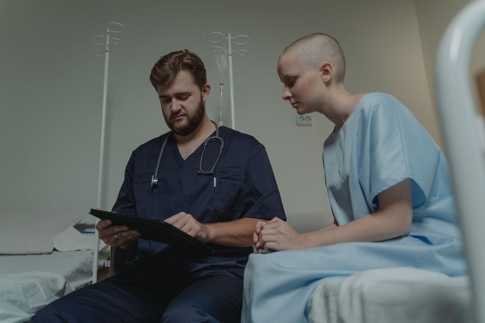 Doctor consulting with patient in hospital room using digital tablet.