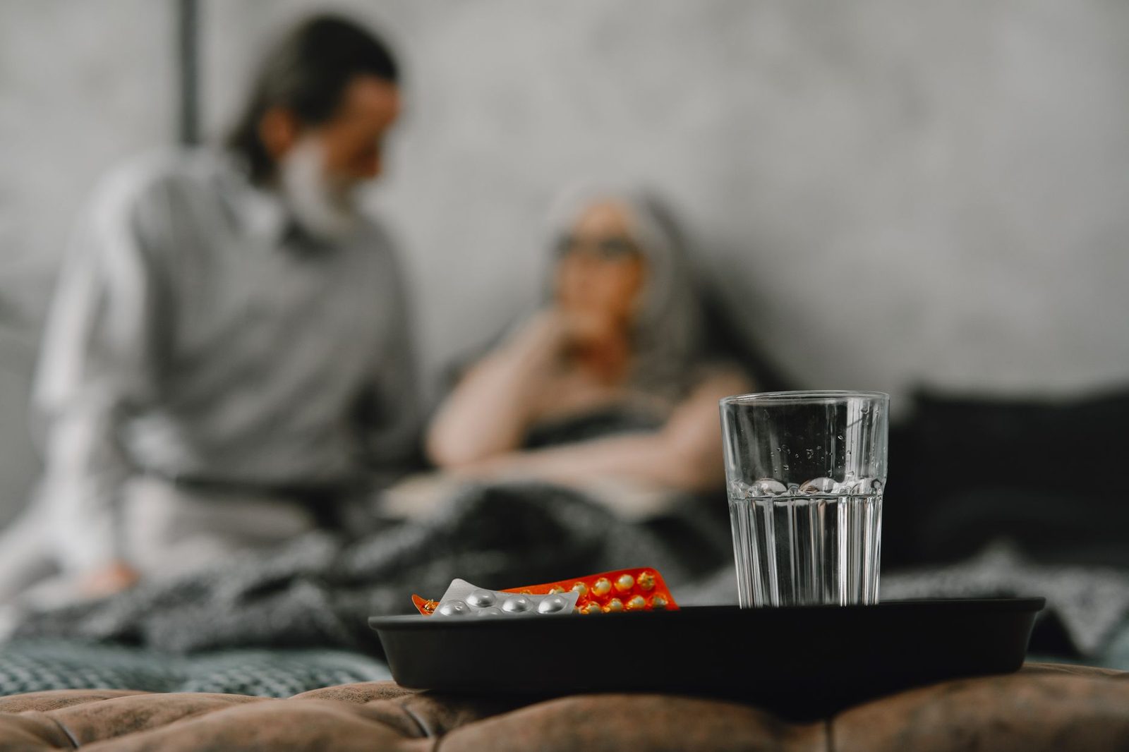Elderly couple reviewing medication bottles together at a kitchen table in a home.