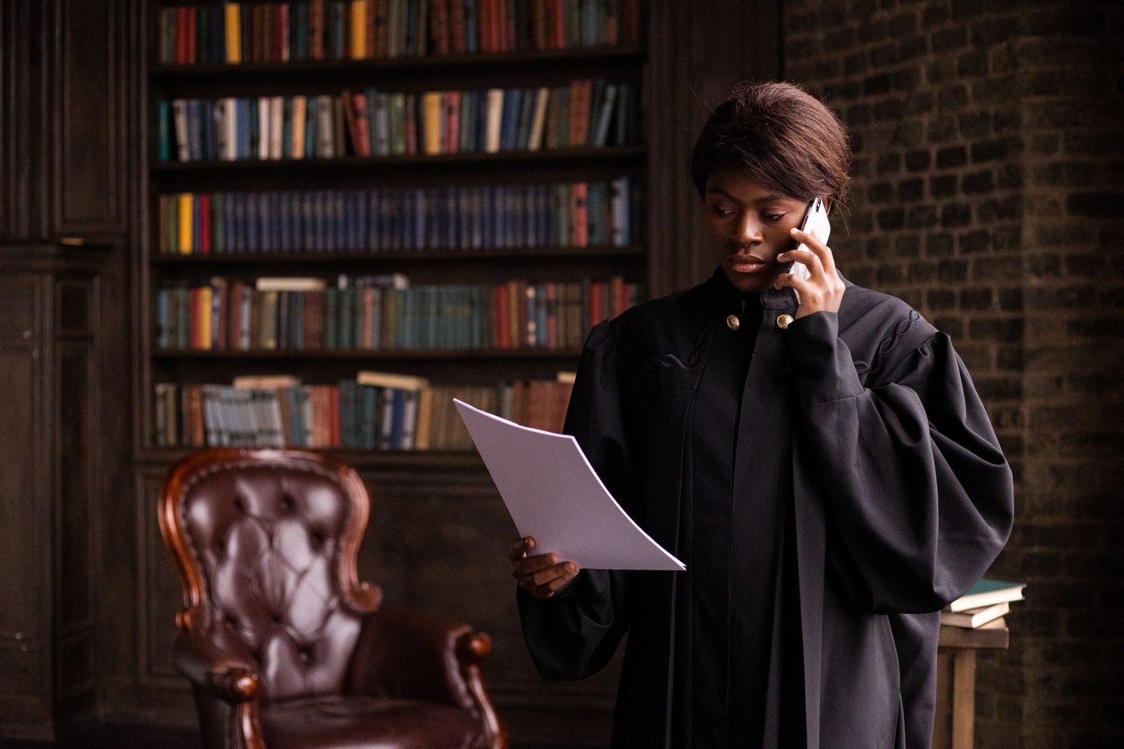 Judge in black robes holds a document while speaking on the phone in a law library.