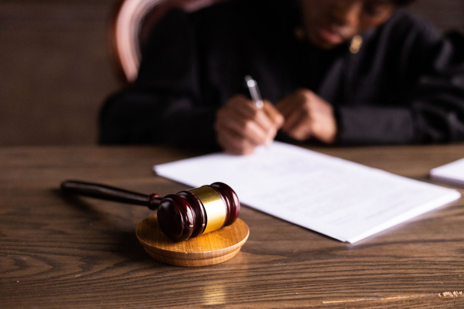 Juez firmando documentos legales con mazo sobre escritorio, representando la ley y justicia.