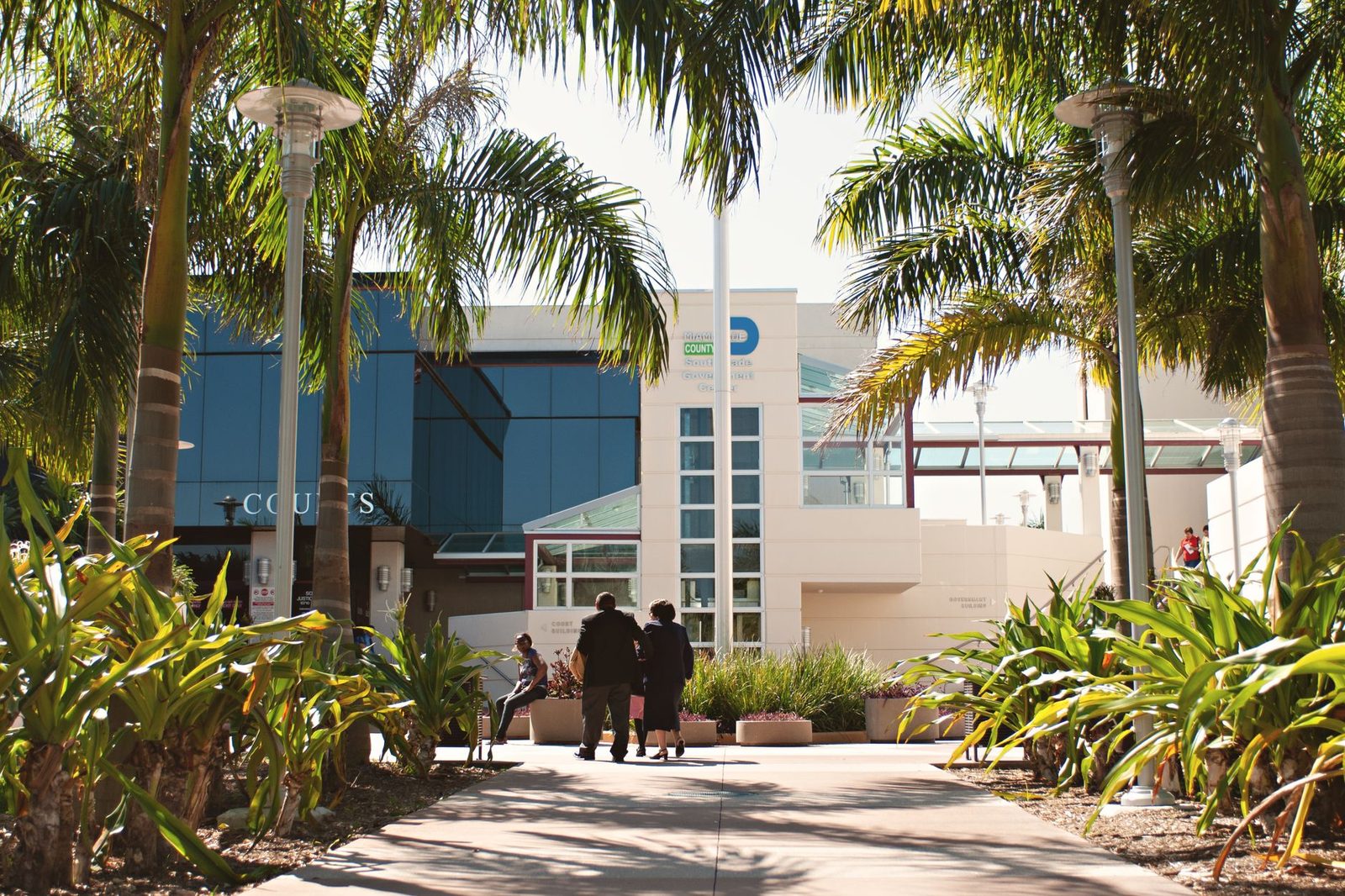 Miami courthouse exterior with palm trees and people walking under a bright blue sky.