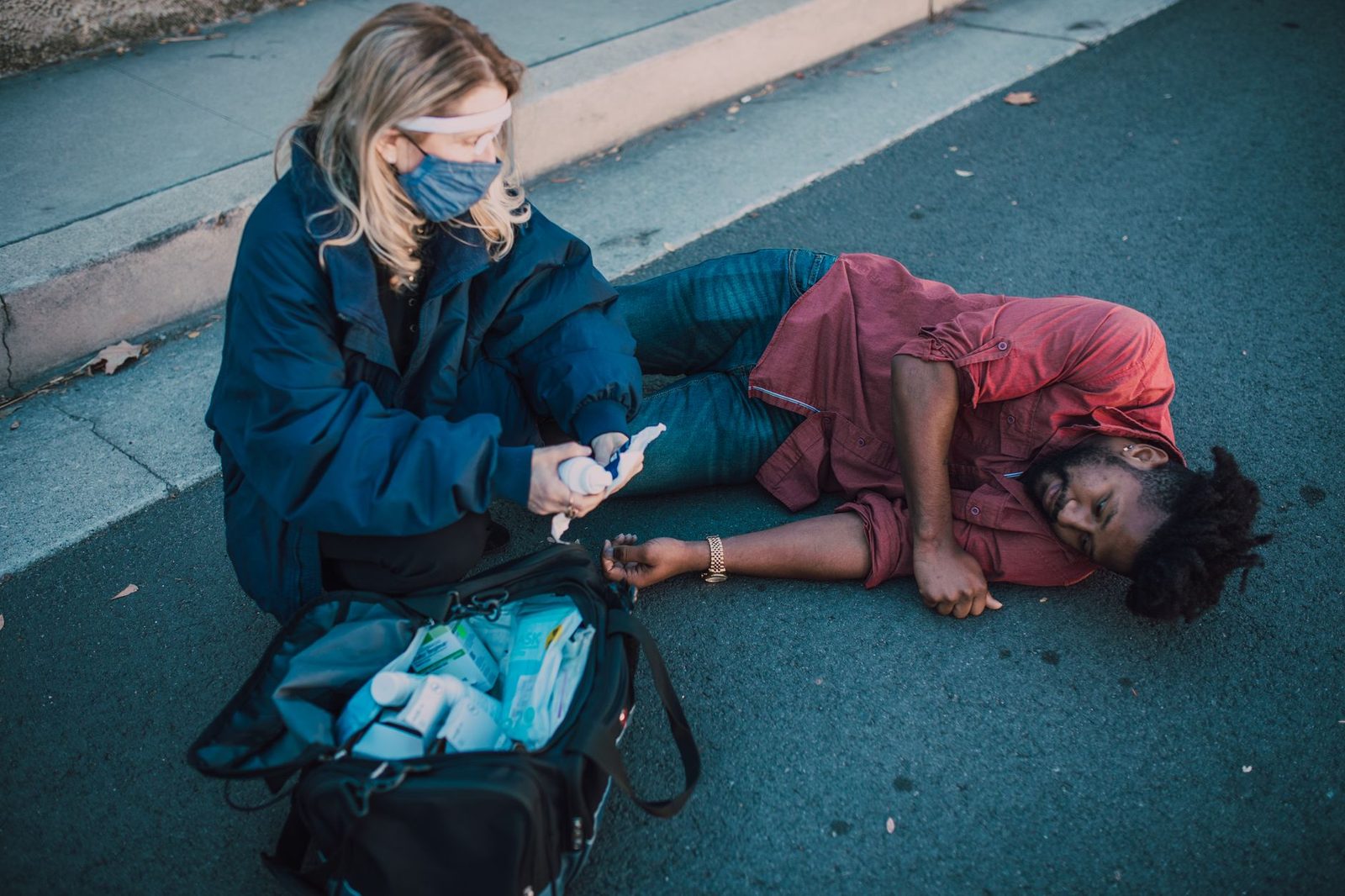 Paramedic kneeling beside an injured man lying on a roadside, providing first aid.