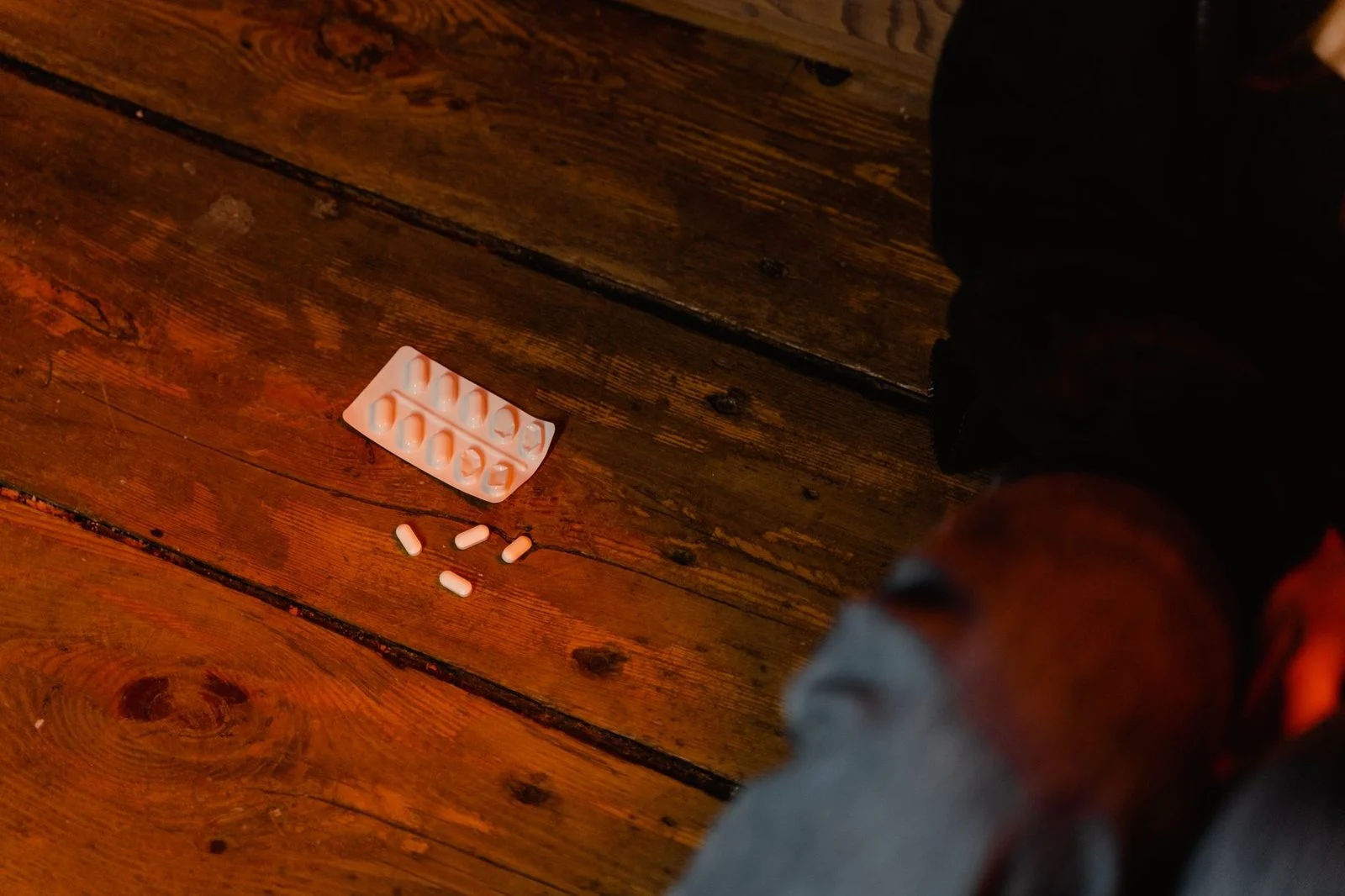 Scattered white pills and an empty blister pack lie on a wooden table.