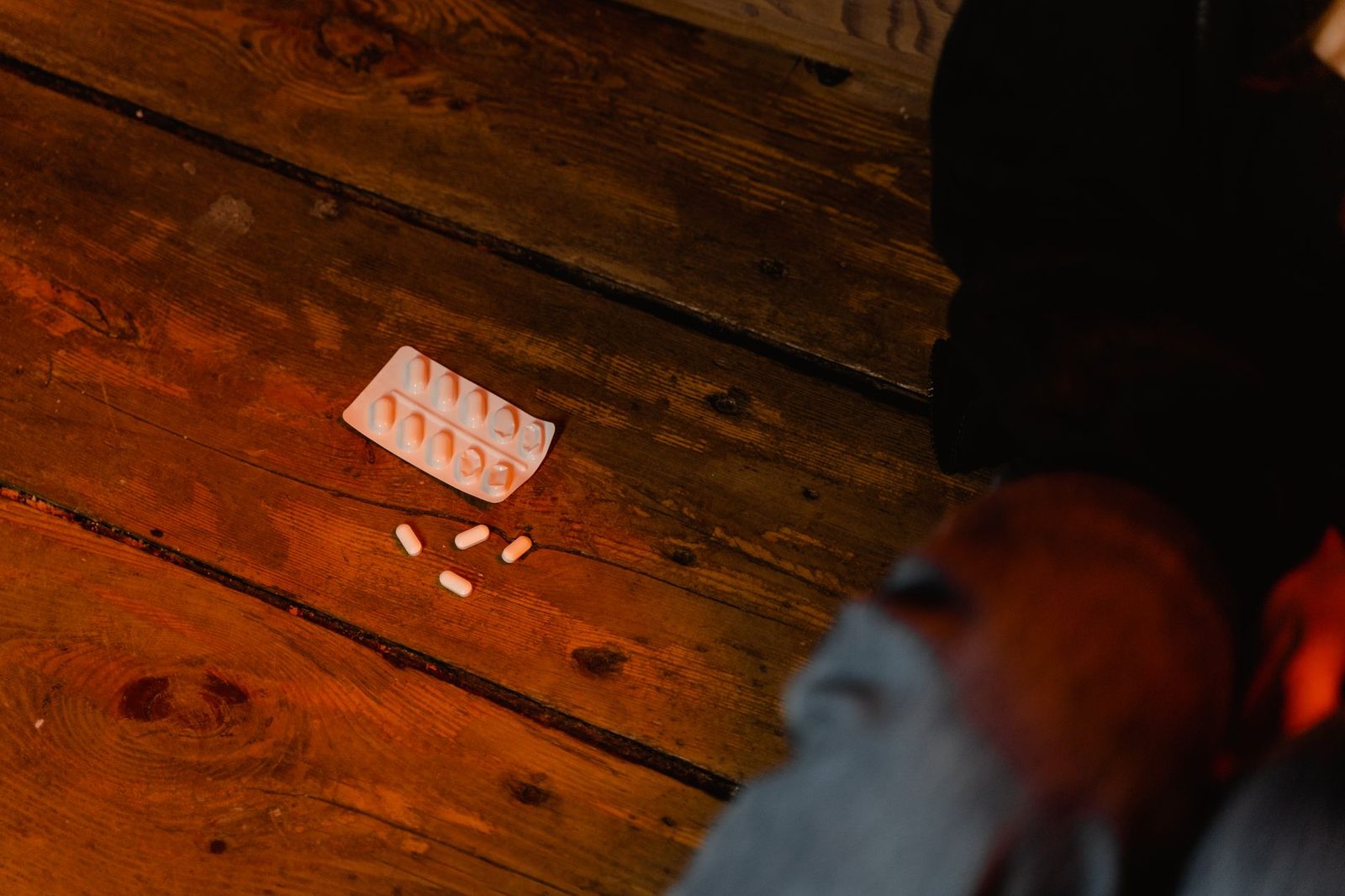Scattered white pills and an empty blister pack lying on a wooden surface.