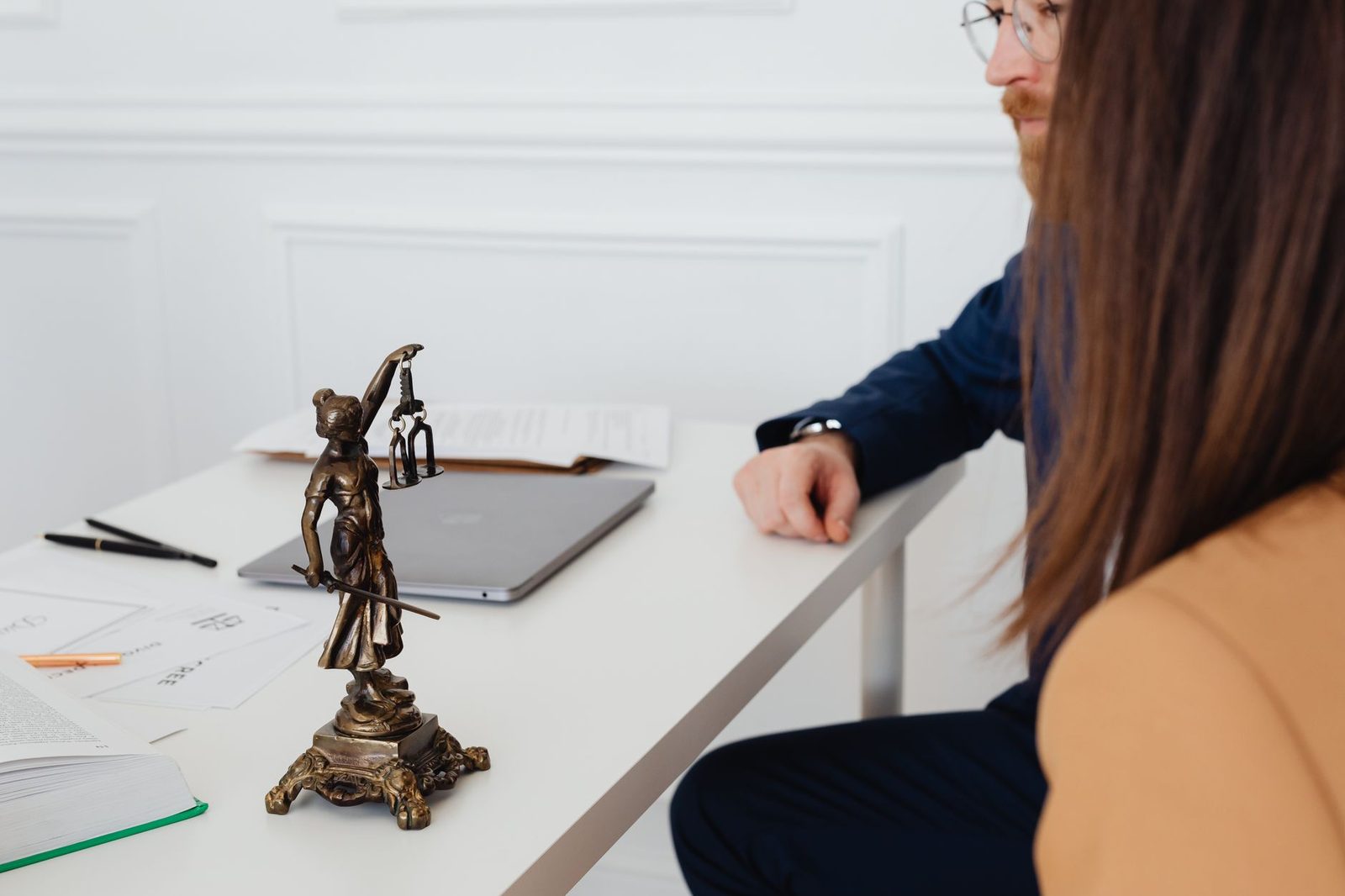 Two lawyers review documents beside a Lady Justice statue in a professional office.