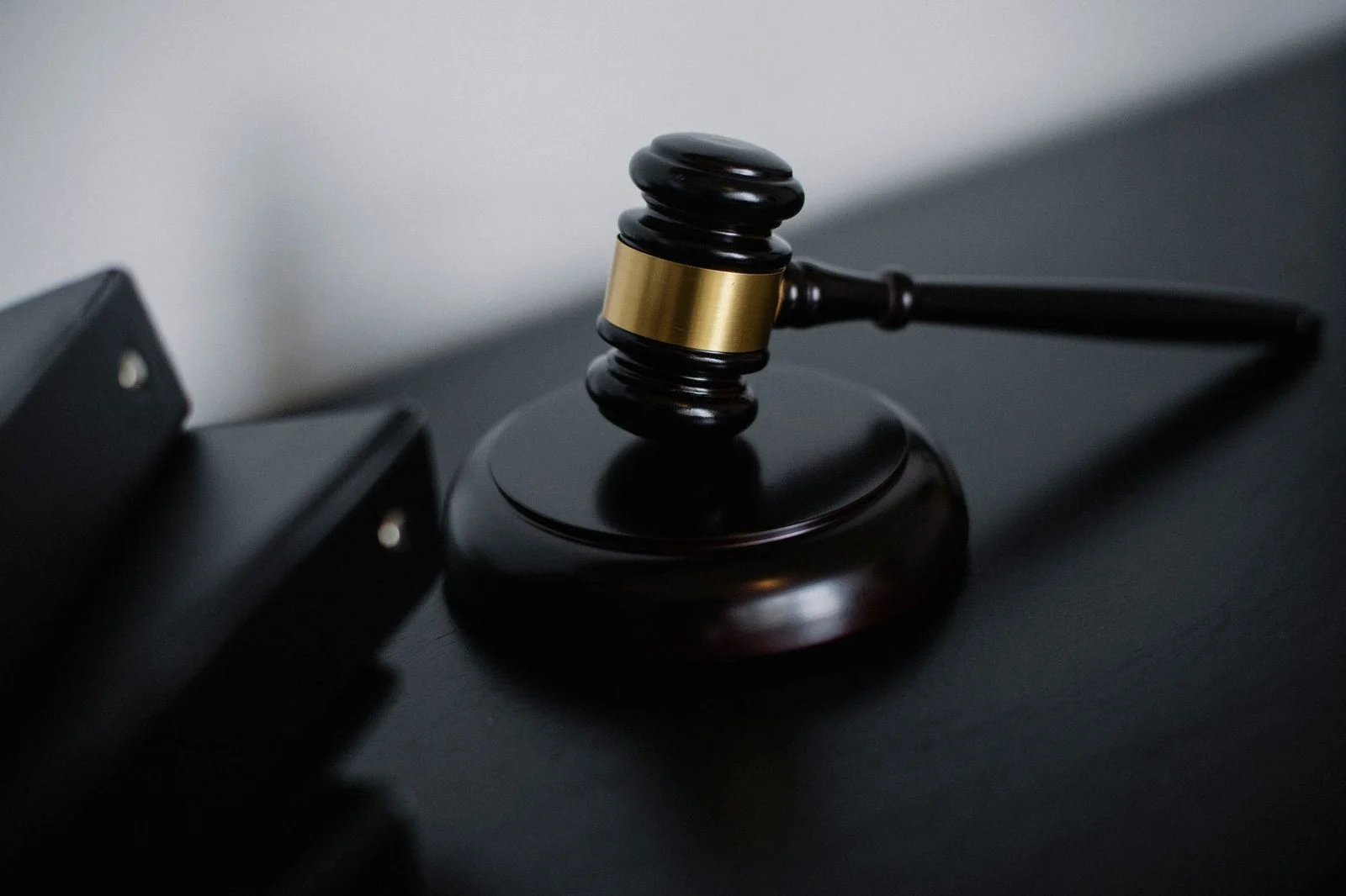 A polished wooden gavel with gold detailing rests on a judge's bench beside stacked case folders.