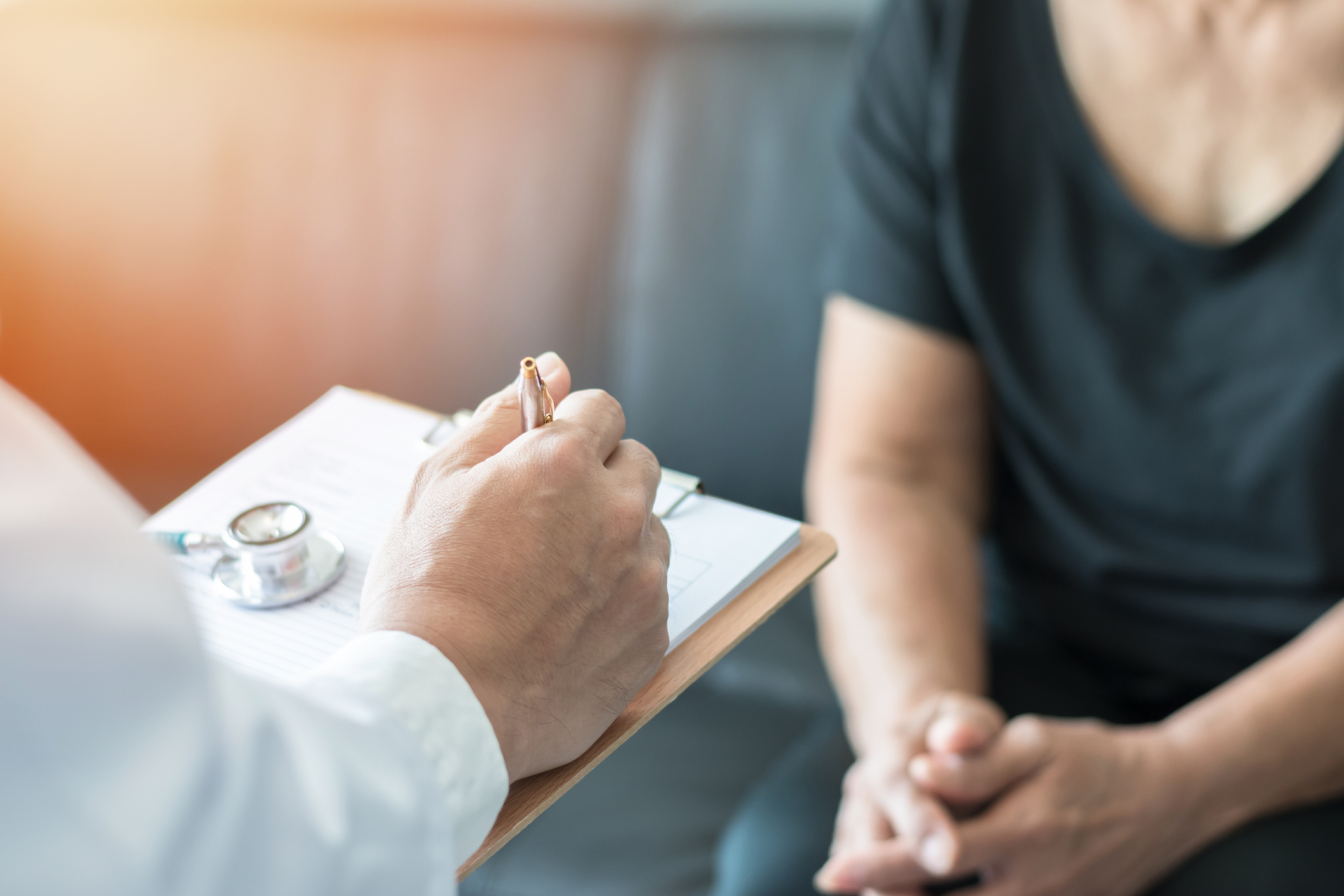 Physician writing in chart for person sitting on chair