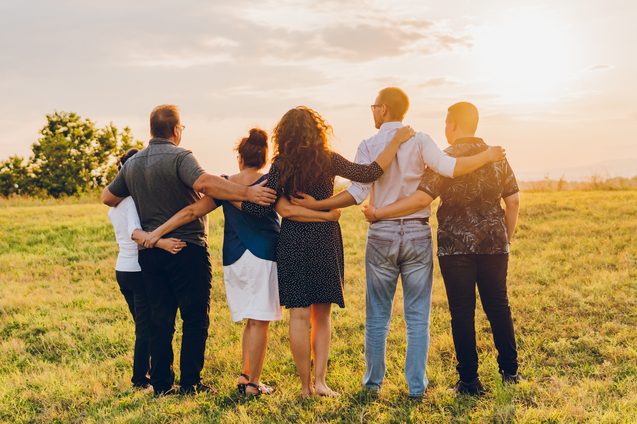 Back view of happy young couple and their parents having fun in a public park during sunset time.
