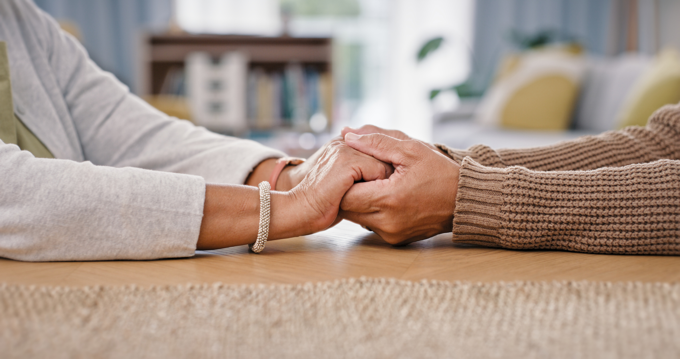 People, holding hands and closeup on table for care love or retirement support, compassion or trust. Couple, partnership and fingers for difficult news or loss comfort, fear solidarity or grief help