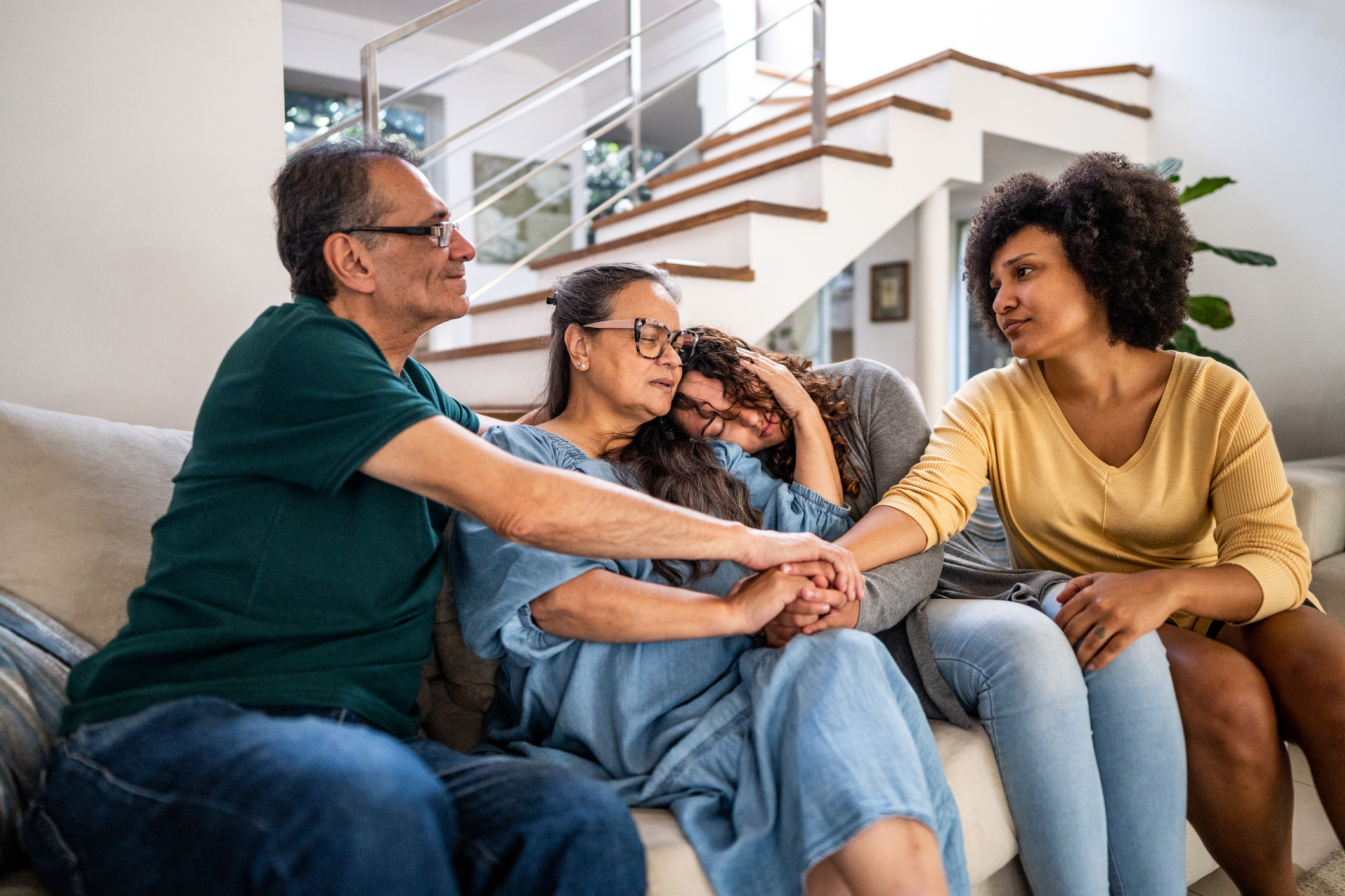 Young woman with her wife being comforted by her parents sitting on sofa in the living room at home
